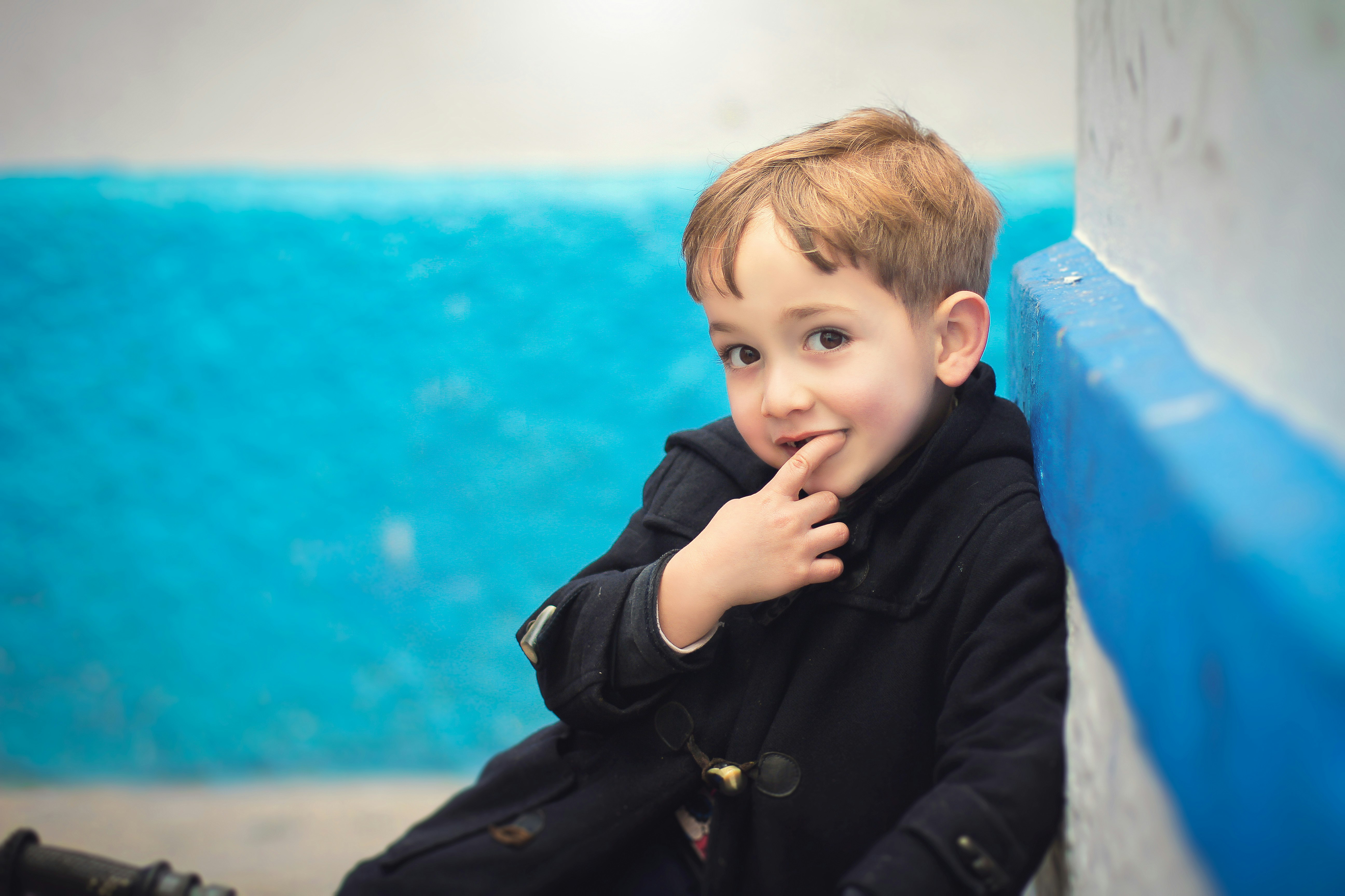 boy in black jacket sitting on blue plastic chair